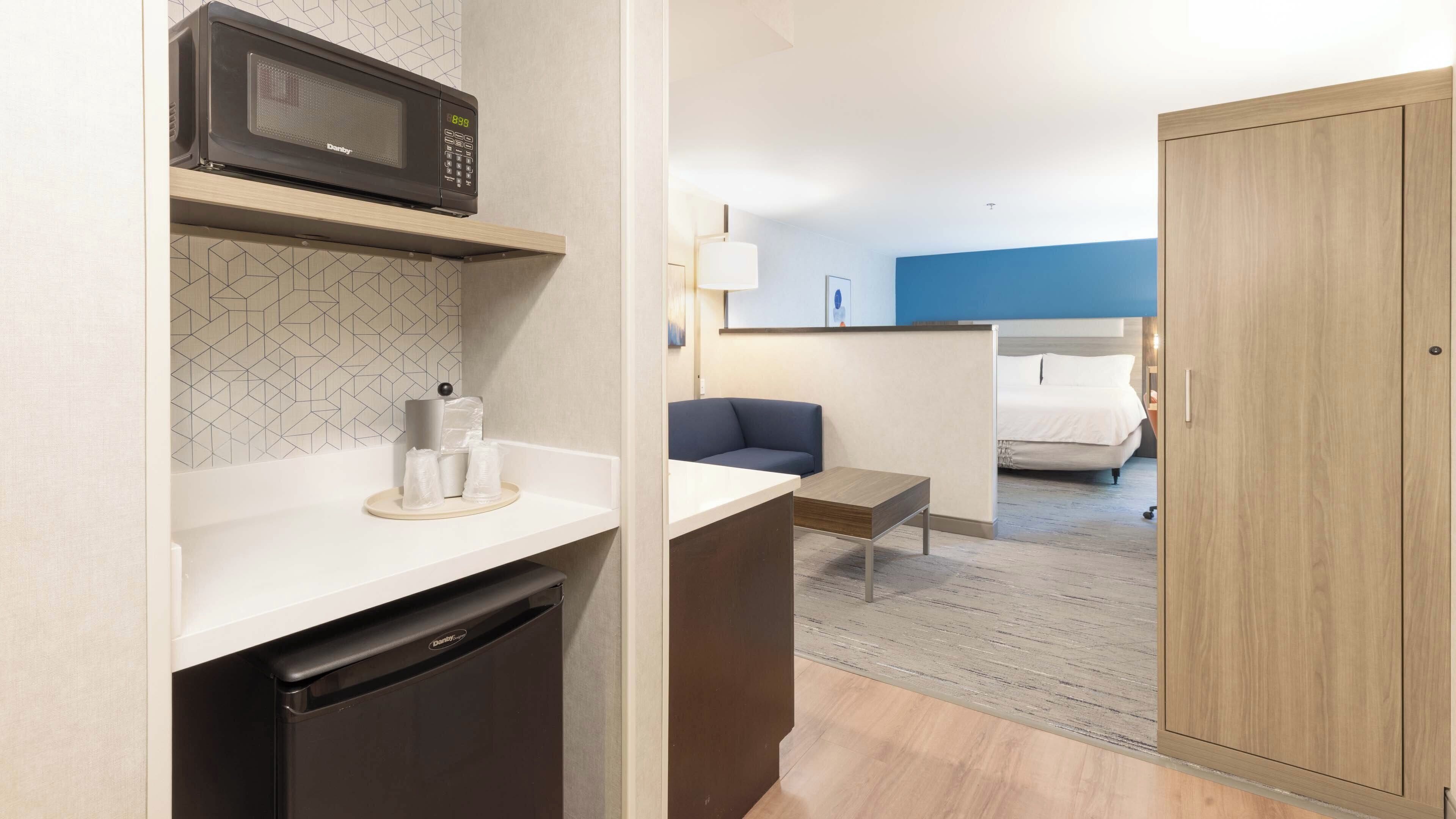 A compact hotel room with a kitchenette, a bed, a sofa, and a wardrobe.