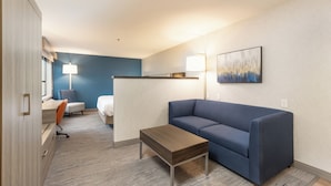 A modern hotel room with a blue accent wall, a sofa, a small table, a desk with a chair, and a painting on the wall. - Holiday Inn Express Bellingham by IHG (Bellingham)