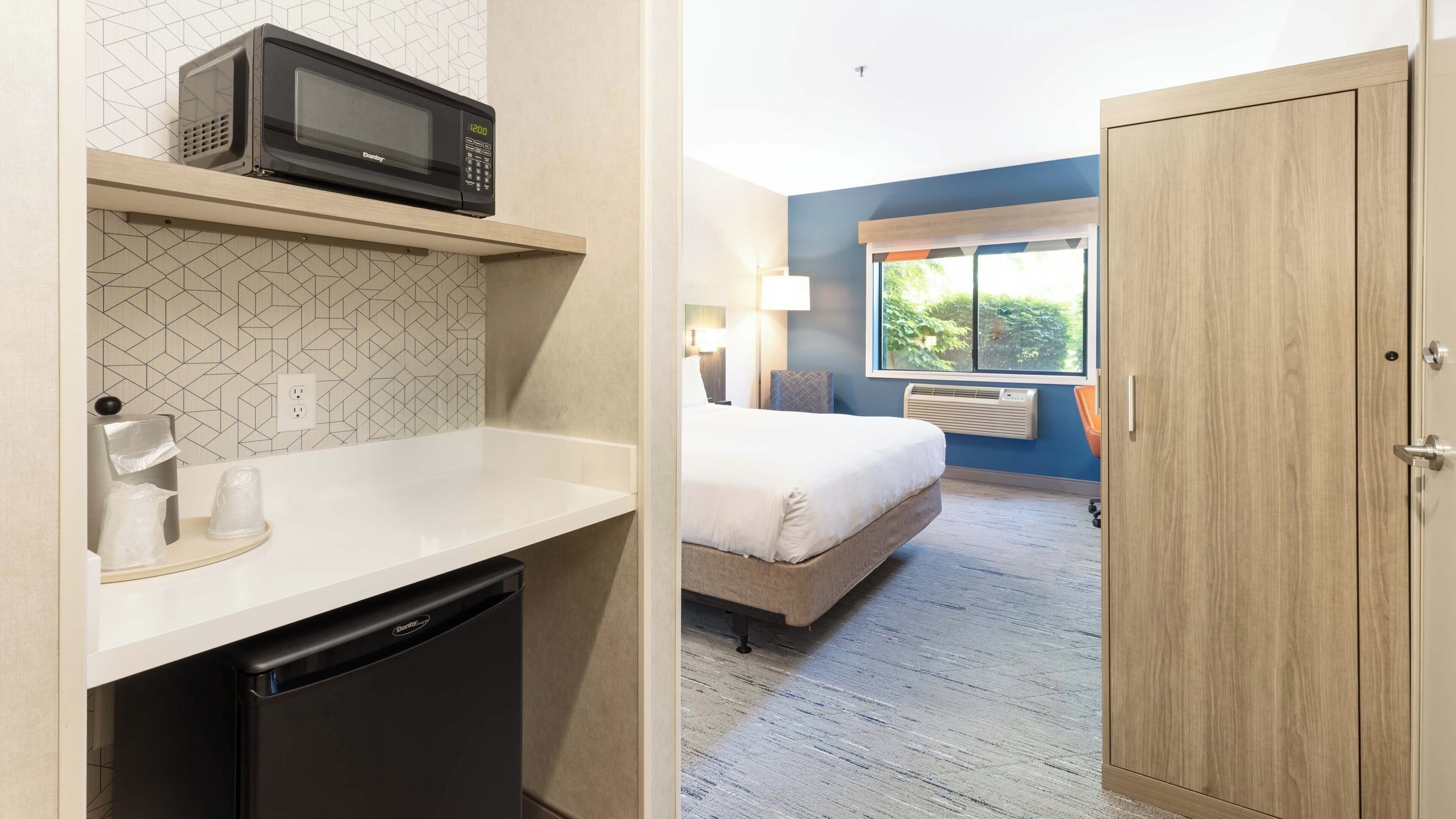 A hotel room with a kitchenette, a bed, a window with a view, and a door.