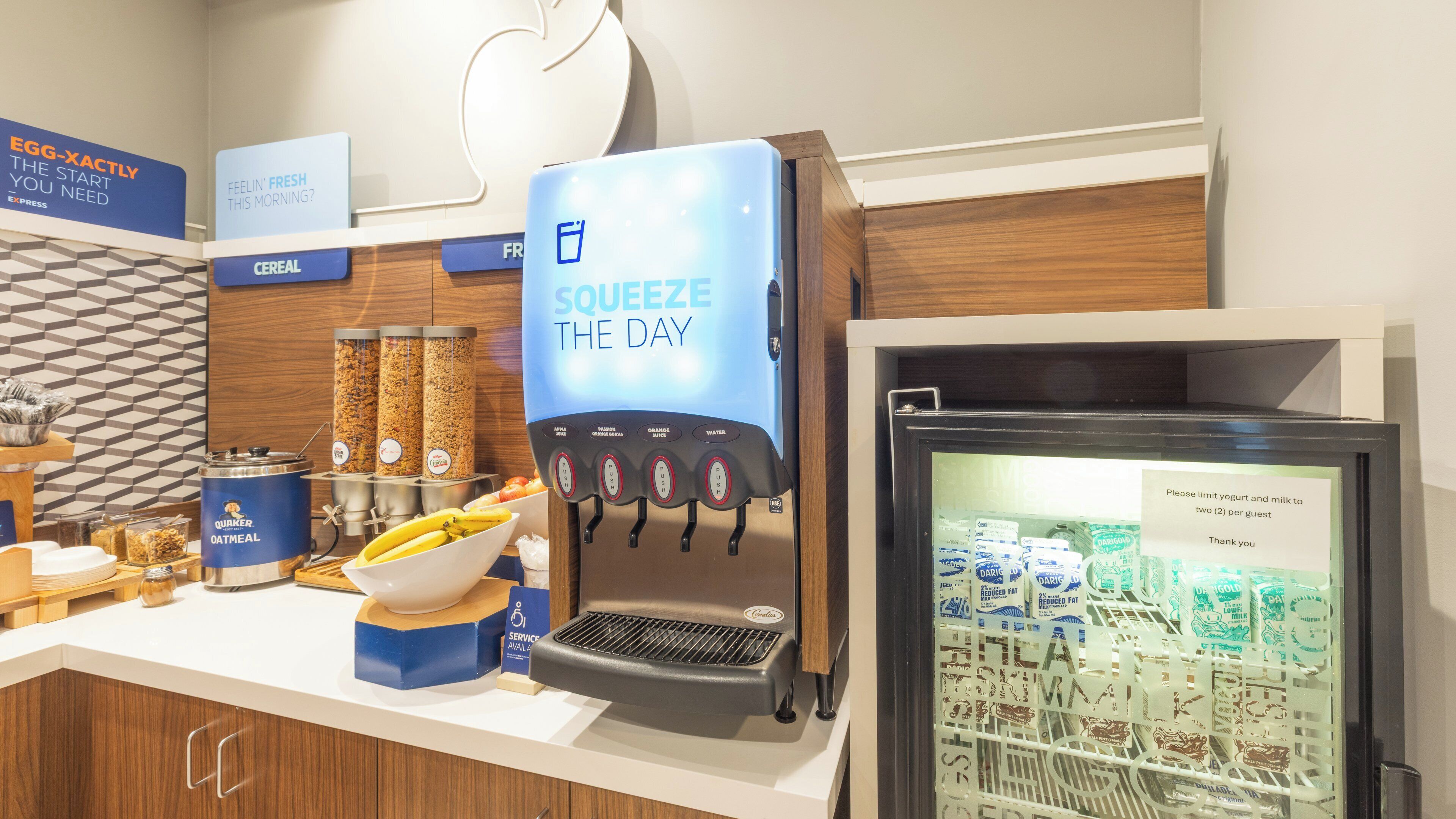 A breakfast station with a coffee machine, cereal dispensers, and a refrigerated display of dairy products.