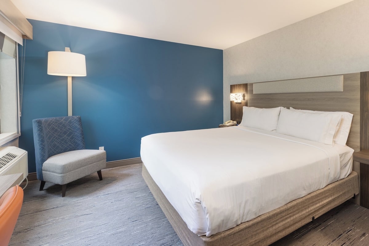 A hotel room with a large bed, a chair, a desk, and a lamp.