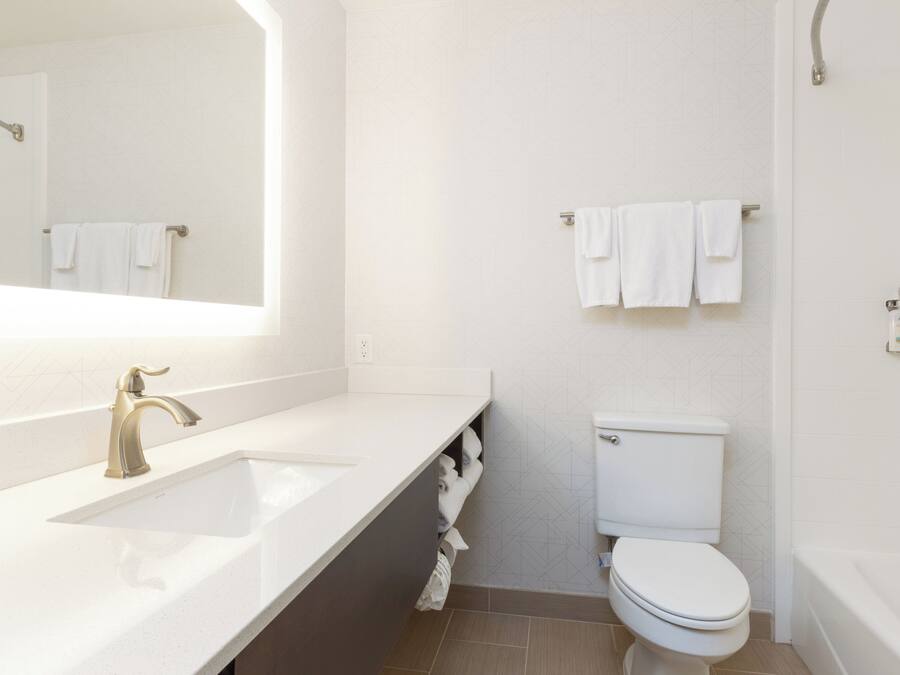 Un baño moderno con lavamanos, espejo, inodoro y toallero.