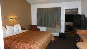 Habitación de hotel con cama, escritorio, silla, televisión y ventana con cortinas.