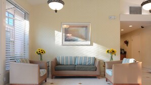 A spacious living area with a sofa and two armchairs, a large window with blinds, and a framed picture on the wall.