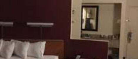 A hotel room with a bed, bedside table, and a small desk with a chair.