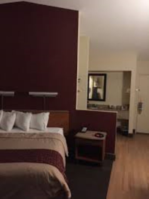 A hotel room with a bed, bedside table, and a small desk with a chair.