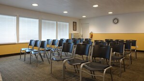 A conference room with rows of chairs, large windows with blinds, a clock on the wall, and a fire extinguisher.