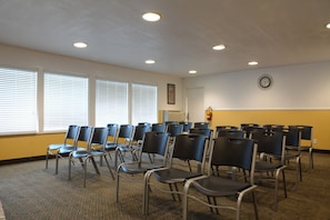 A conference room with rows of chairs, large windows with blinds, a clock on the wall, and a fire extinguisher.
