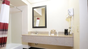 Un baño con ducha, lavabo con espejo, teléfono y cafetera.