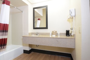 A bathroom with a shower, a sink with a mirror, a telephone, and a coffee maker.