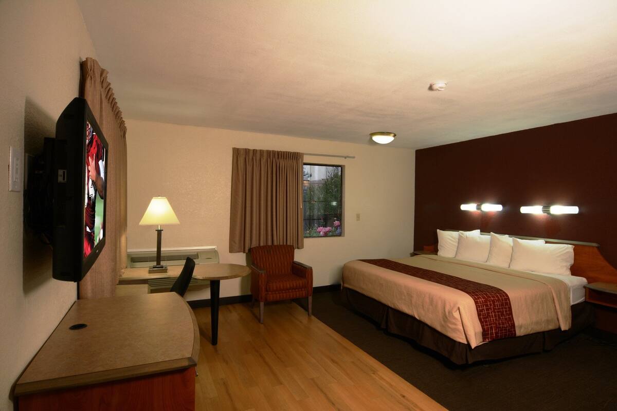 Hotelkamer met een bed, bureau, stoel, televisie en raam met gordijnen.