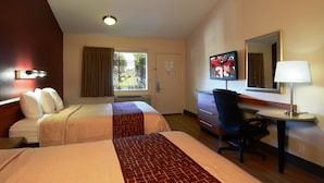 Habitación de hotel con dos camas, un escritorio, una silla, una lámpara, un televisor y una ventana con cortinas.