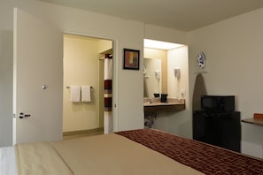 A hotel room with a bed, a bathroom with a shower, a hairdryer, and a microwave.