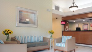 A hotel lobby with a reception desk, a sofa, two armchairs, and a painting on the wall.