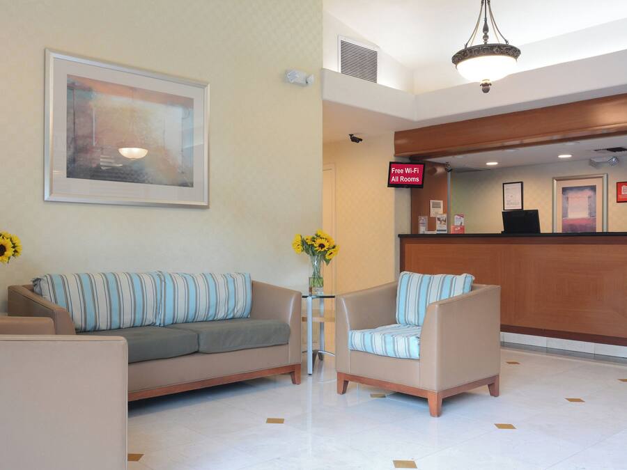 A hotel lobby with a reception desk, a sofa, two armchairs, and a painting on the wall.