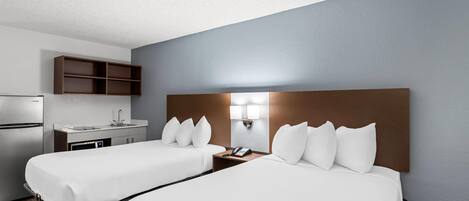 A hotel room with two beds, a kitchenette, and a bathroom.