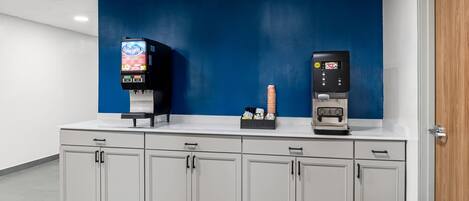 A self-service beverage station with two machines, a blue wall, and a white counter with cabinets.
