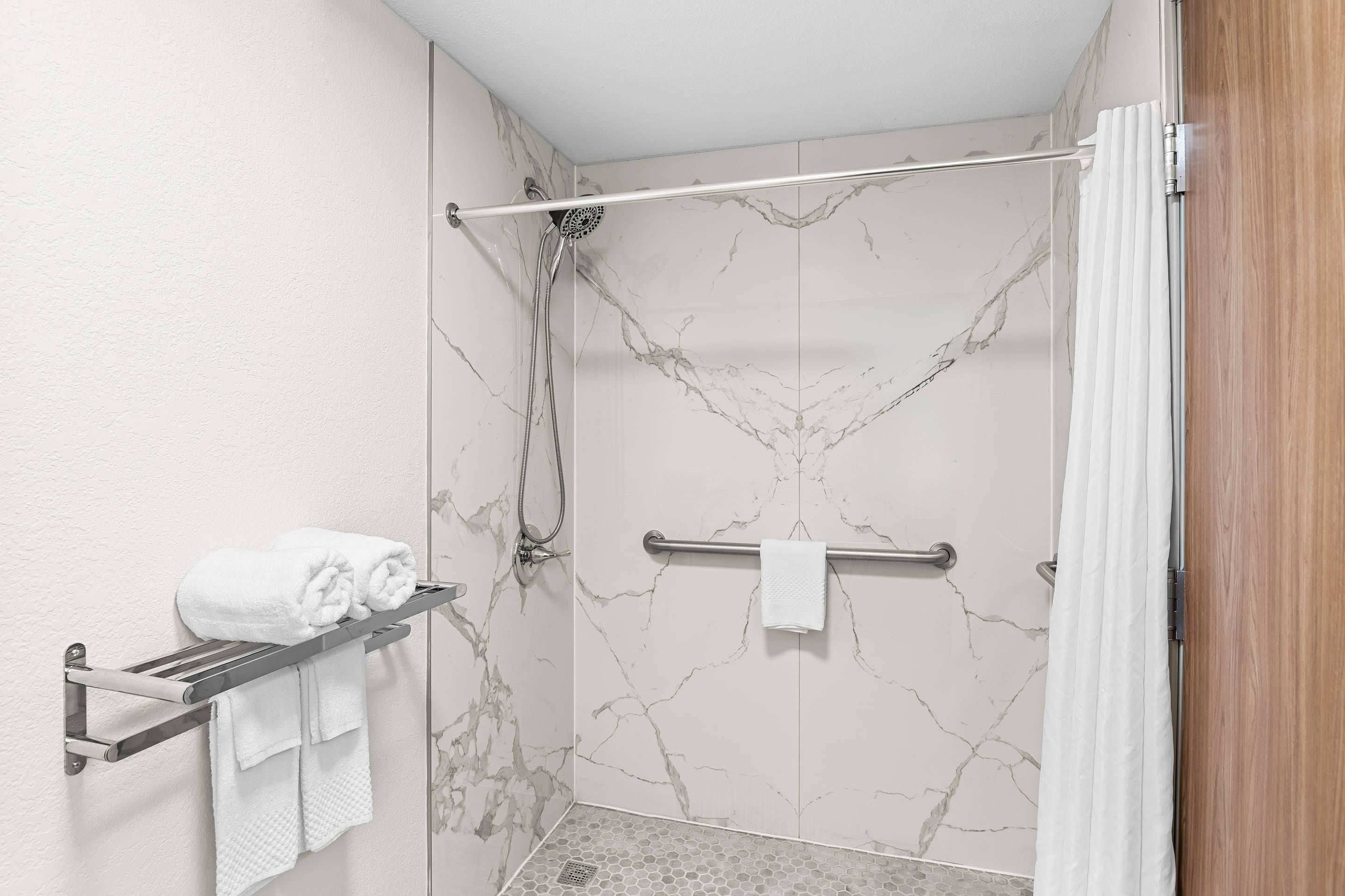 A bathroom with a shower, marble walls, a towel rack, and a wooden door.