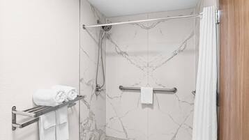 A bathroom with a shower, marble walls, a towel rack, and a wooden door.