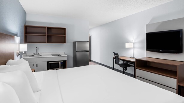 A hotel room with a bed, a desk, a chair, a TV, a mini-fridge, a microwave, and a kitchenette with a fridge and a sink. - Suburban Studios Chester (Chester)