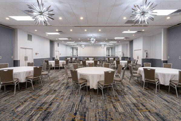 A large conference room with multiple round tables and chairs, carpeted flooring, and modern ceiling lights.