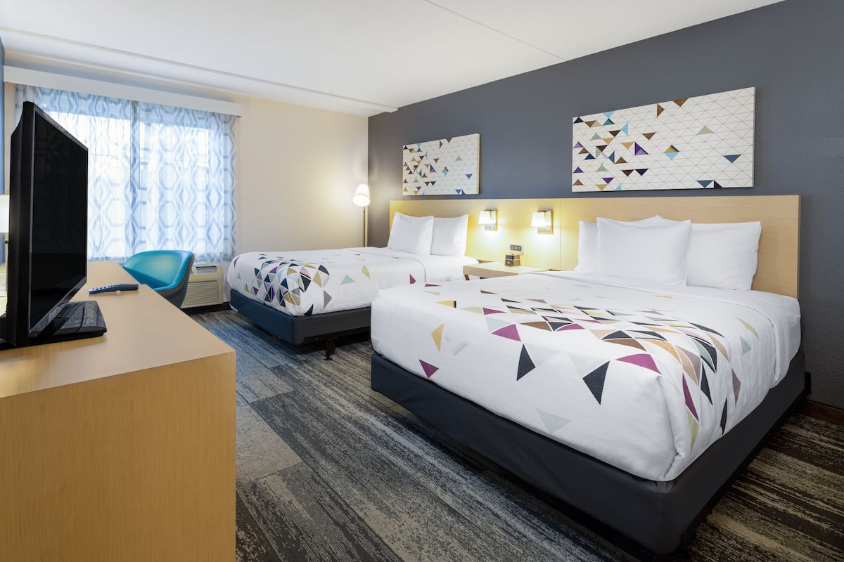 Ein Hotelzimmer mit zwei Betten, einem Schreibtisch, einem Fernseher und einem Vorhangfenster.