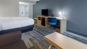 A hotel room with a bed, a desk with a computer and TV, a chair, and a small table.