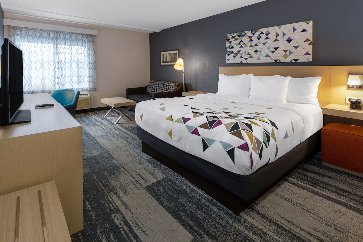 Ein Hotelzimmer mit einem großen Bett, einem Schreibtisch, einem Sessel, einem Fernseher und einer Wand mit geometrischem Muster.