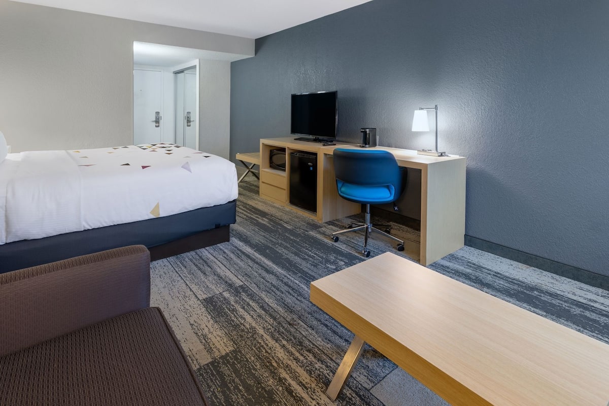 Ein Hotelzimmer mit einem Bett, einem Schreibtisch mit Stuhl, einem Fernseher und einer Lampe.