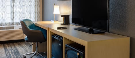 Et moderne hotelværelse med skrivebord i træ, et fladskærms-tv, en mikrobølgeovn, en kaffemaskine og en stol.