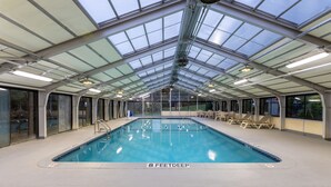 An indoor swimming pool with a glass ceiling, clear signage indicating depth, and lounge chairs along the sides. - Baymont by Wyndham White Plains - Elmsford (Elmsford)