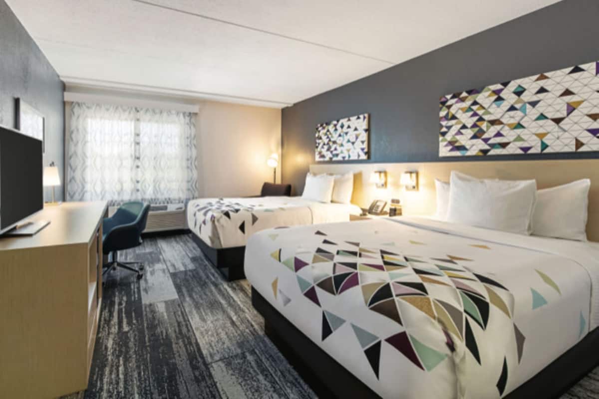 Ein Hotelzimmer mit Schreibtisch, zwei Betten, einem Fernseher und einer Wand mit Muster.