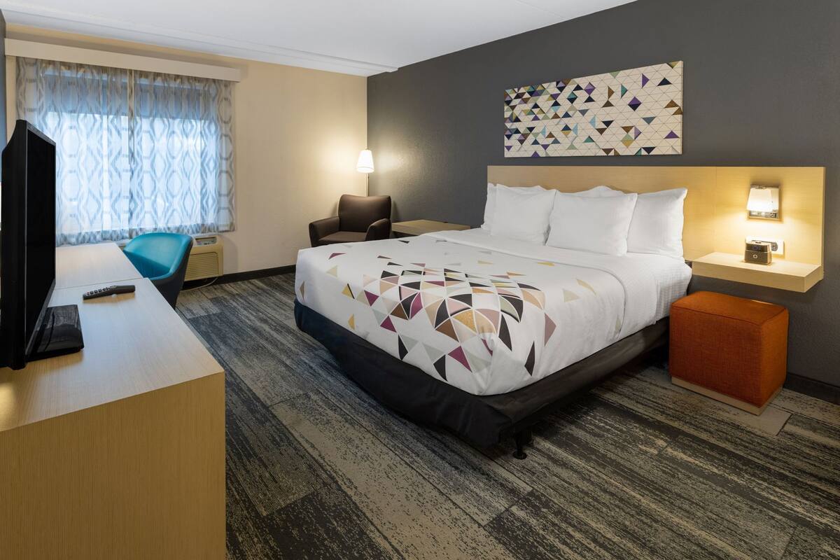 Ein Hotelzimmer mit Bett, Schreibtisch, Stuhl, Fernseher, Lampe und einem Bild an der Wand.