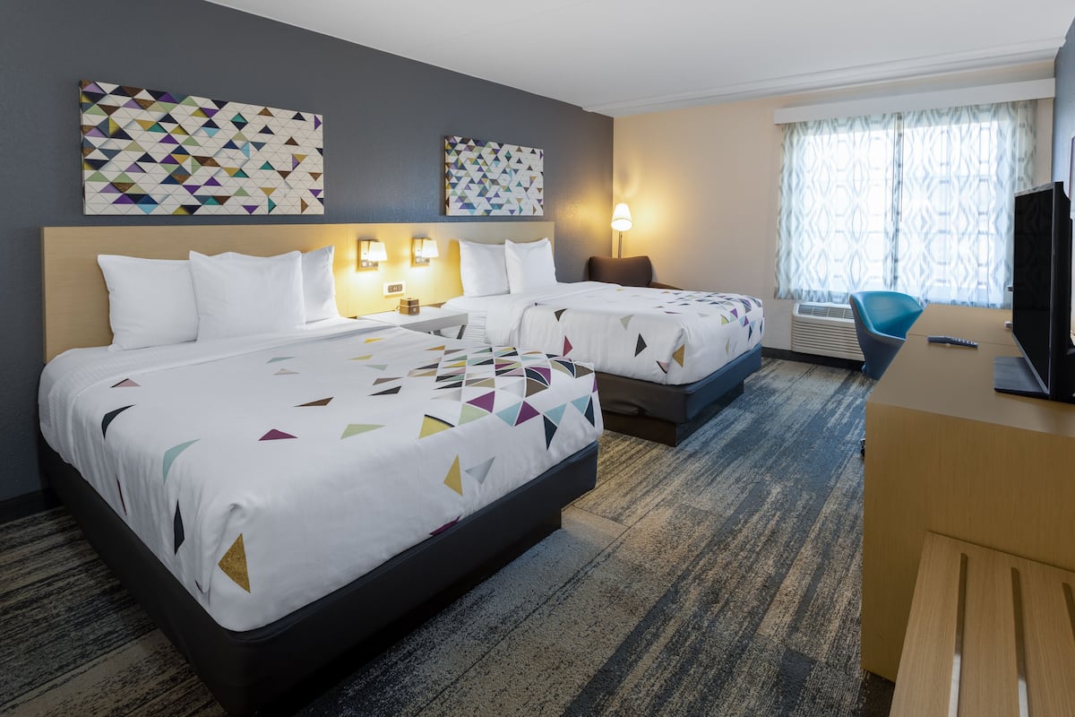 Ein Hotelzimmer mit zwei Betten, einem Schreibtisch, einem Fernseher und Bildern an den Wänden.
