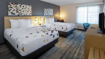 A hotel room with two beds, a desk, a TV, and artwork on the walls.