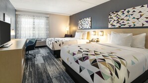 A hotel room with a large bed, a desk, and a chair. There is a window with curtains and a wall with a geometric patterned design. - Baymont by Wyndham White Plains - Elmsford (Elmsford)