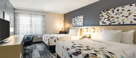 A hotel room with a large bed, a desk, and a chair. There is a window with curtains and a wall with a geometric patterned design.