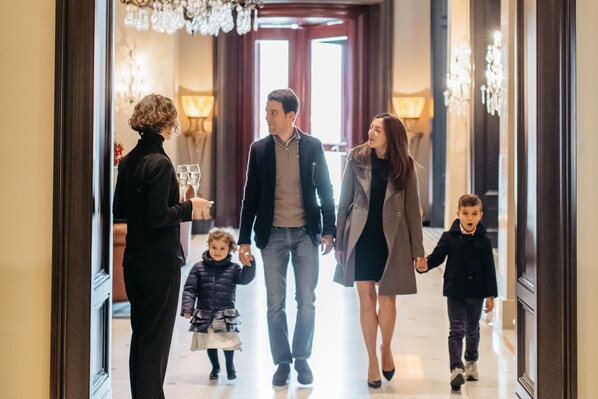 Una familia caminando por un pasillo con candelabros y un ventanal grande al fondo.