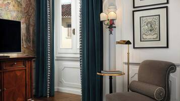 A room with a wooden cabinet, a television, a chair with a patterned cushion, a floor lamp, and framed artwork on the wall.