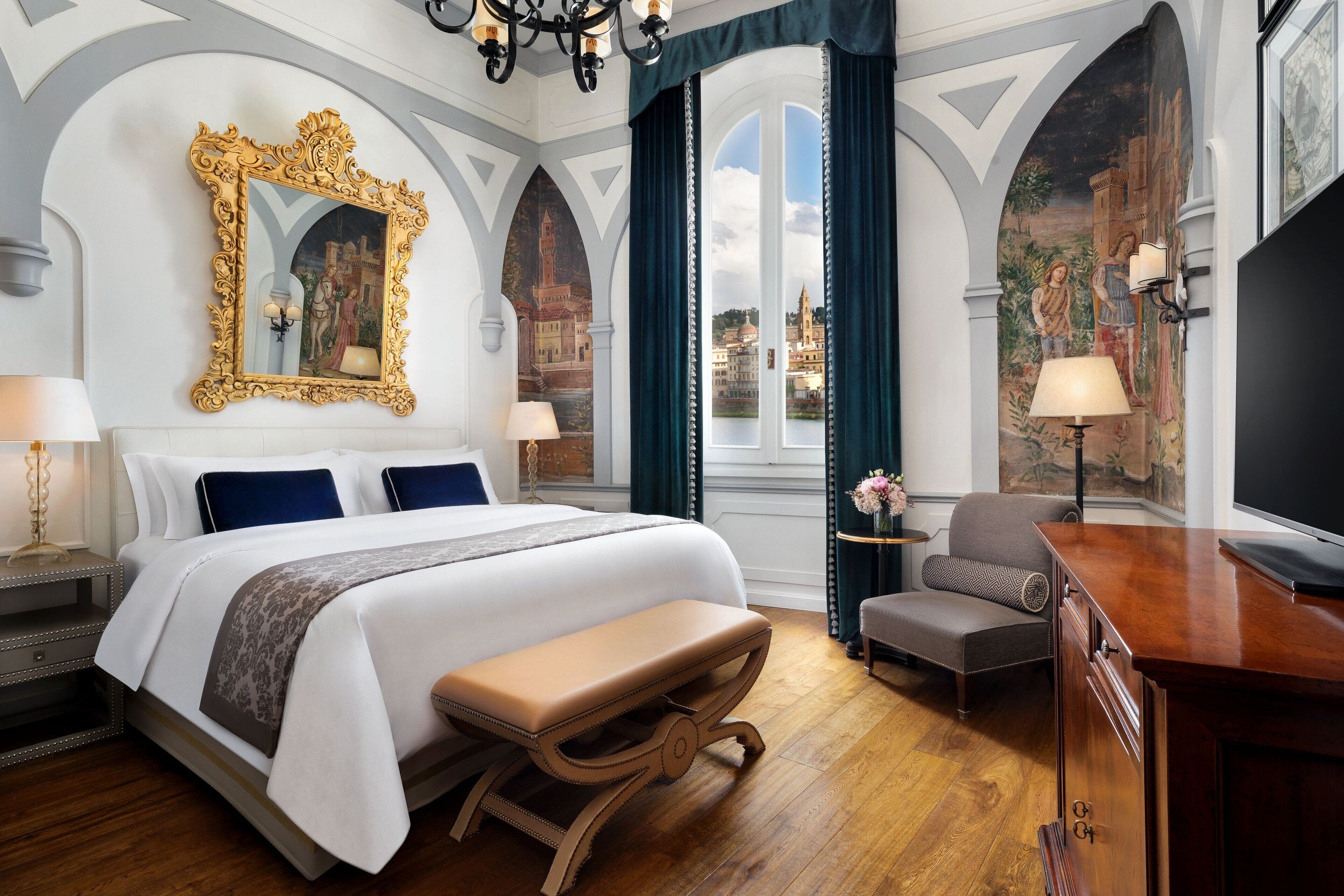 Ein luxuriöses Hotelzimmer mit einem großen Bett, einer Bank, einem Schreibtisch und Blick auf die Skyline der Stadt.