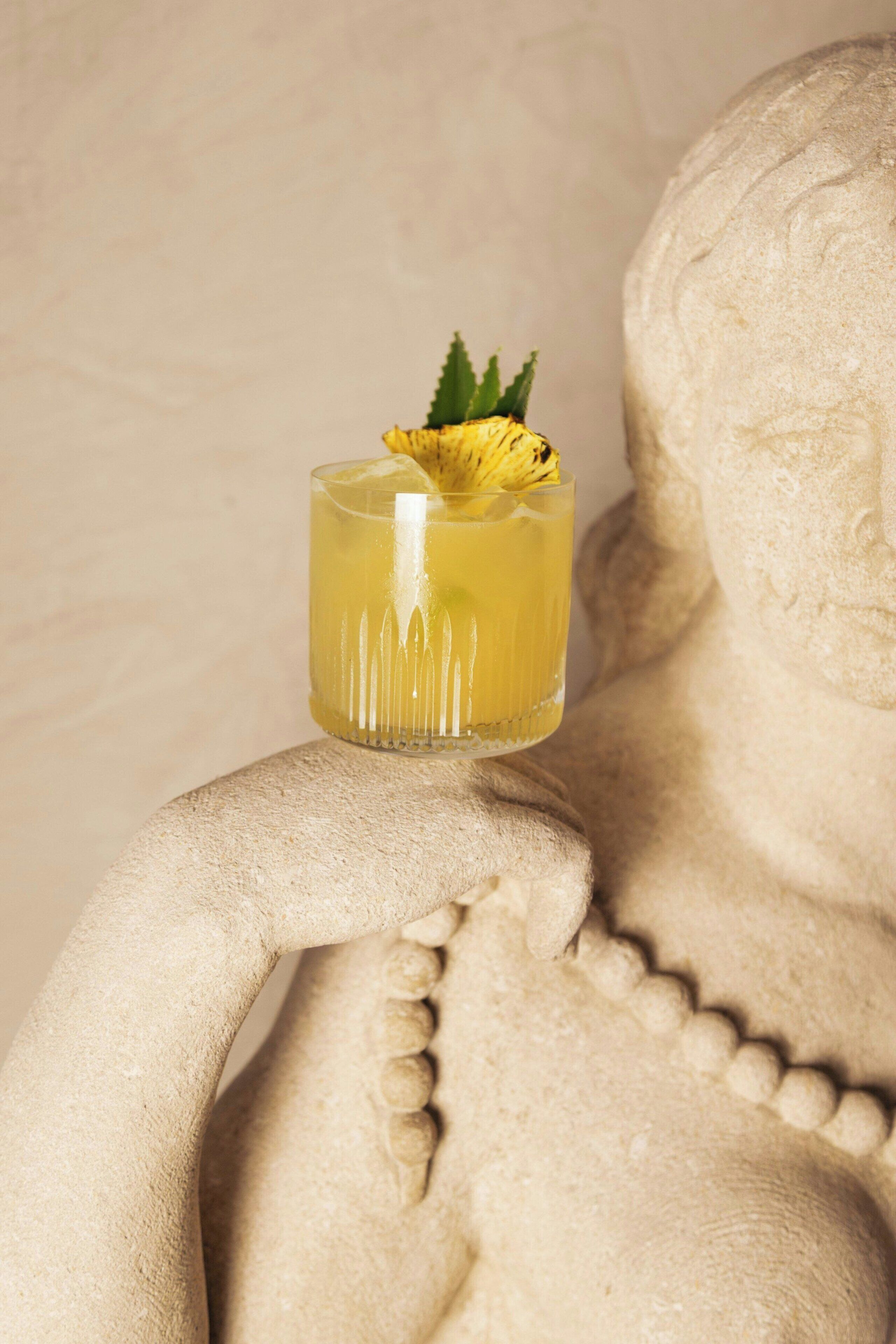 A clear glass with a yellow liquid and a garnish, placed on a textured surface.