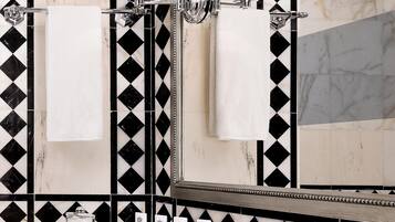 A bathroom with a black and white tiled wall, a large mirror, two wall-mounted lamps, a white sink, and a towel rack with two towels.