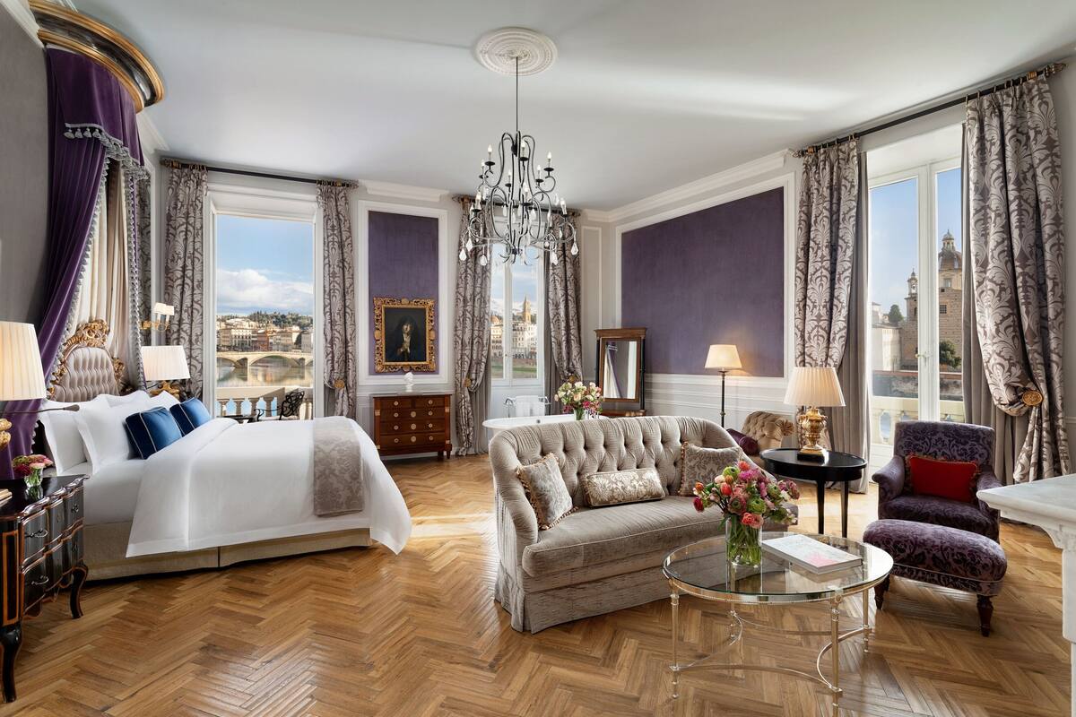 A luxurious hotel room with a large bed, a sofa, a round coffee table, and a view of the city.