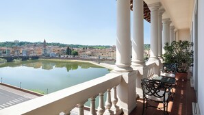 A balcony with a view of a river and buildings, featuring a table and chairs.
