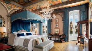 A luxurious bedroom with a large bed, ornate ceiling, and a view of a dome through a large window.