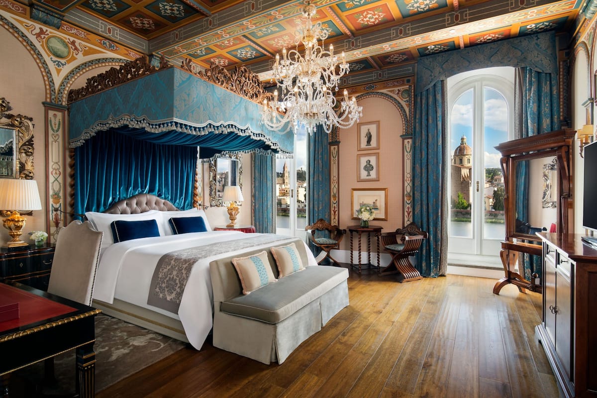 A luxurious bedroom with a large bed, ornate ceiling, and a view of a dome through a large window.