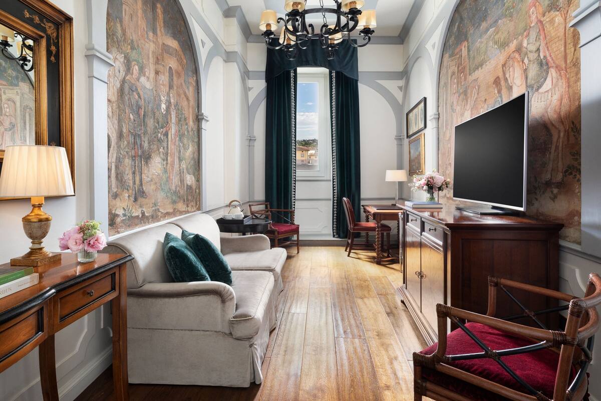 A room with a wooden floor, a sofa, a chair, a TV, and a painting on the wall.