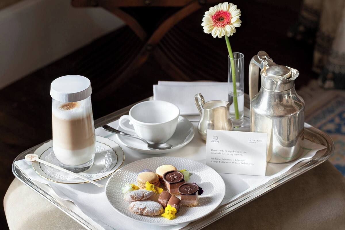 A tray with a milk glass, a cup, a sugar bowl, a pitcher, a plate with pastries, and a flower.