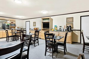 A spacious dining area with multiple tables and chairs, a kitchen area with a microwave, refrigerator, and various appliances, and a television mounted on a wooden cabinet.