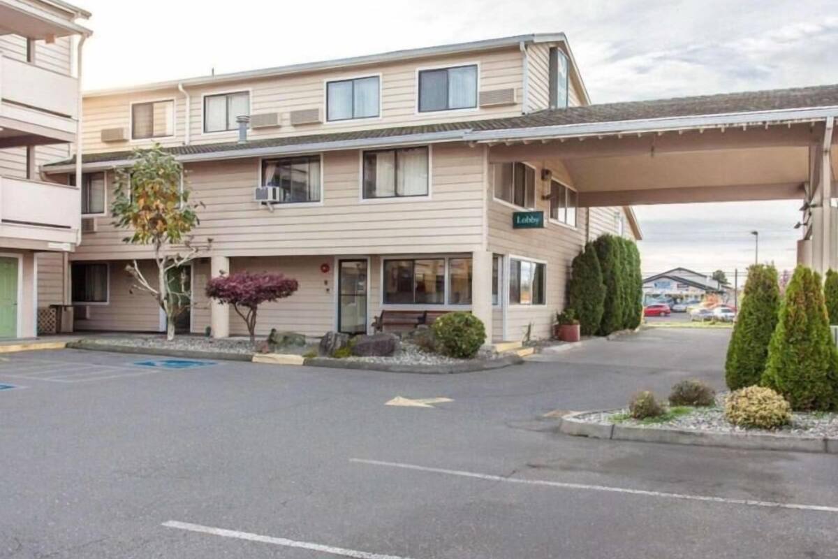 A motel with a covered parking area, a lobby entrance, and a row of windows on the building.